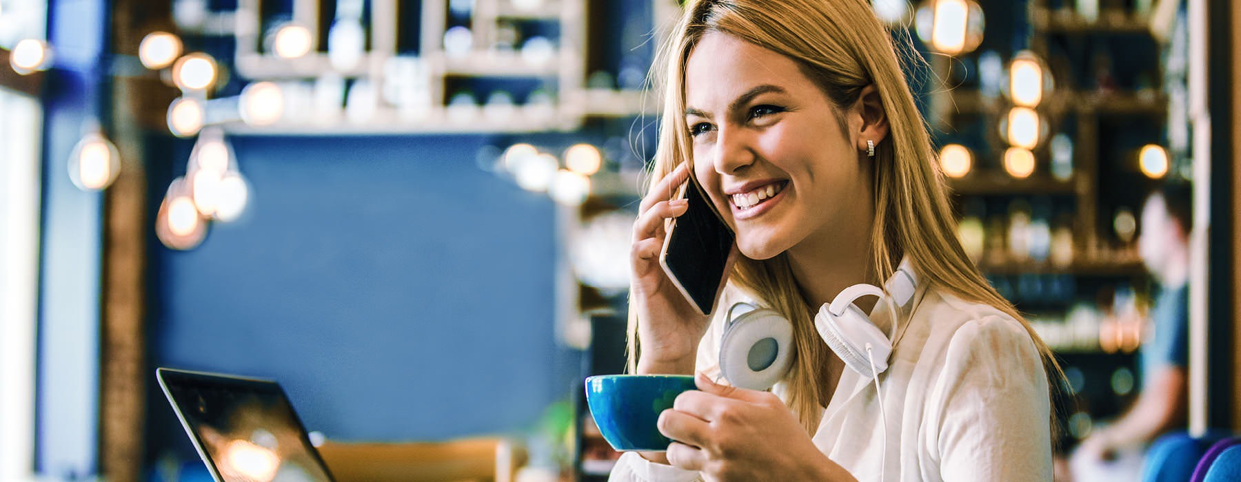 smiling woman on phone holds a cup of espresso in cafe